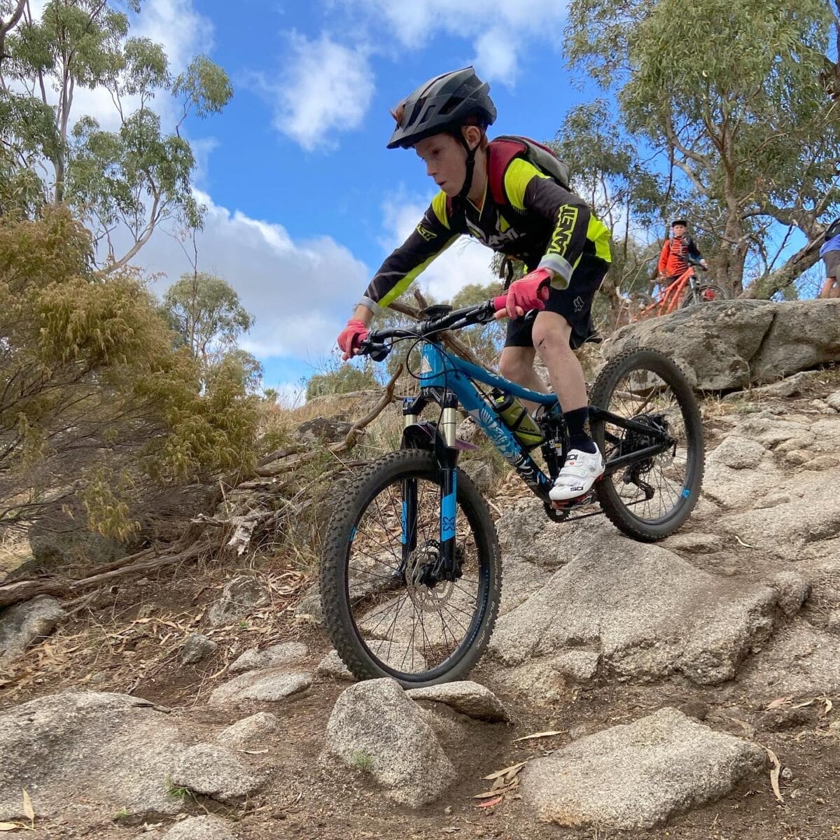 Mountain biker riding technical rocky trail section during coaching session